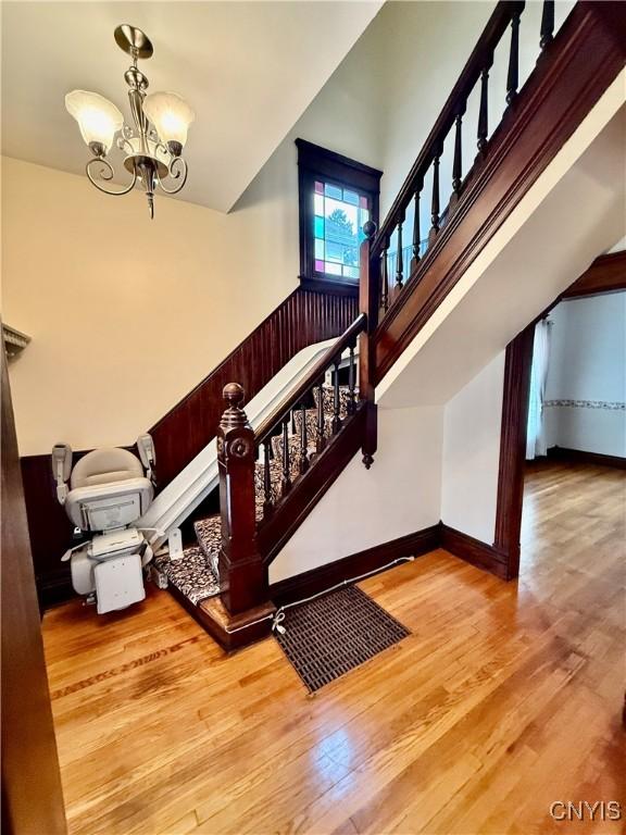 stairs with an inviting chandelier, baseboards, wood finished floors, and high vaulted ceiling