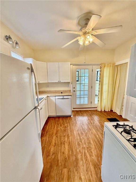 kitchen with wood finished floors, white appliances, ceiling fan, light countertops, and white cabinetry