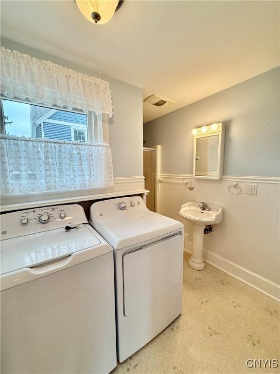 washroom featuring washing machine and clothes dryer, laundry area, wainscoting, and baseboards
