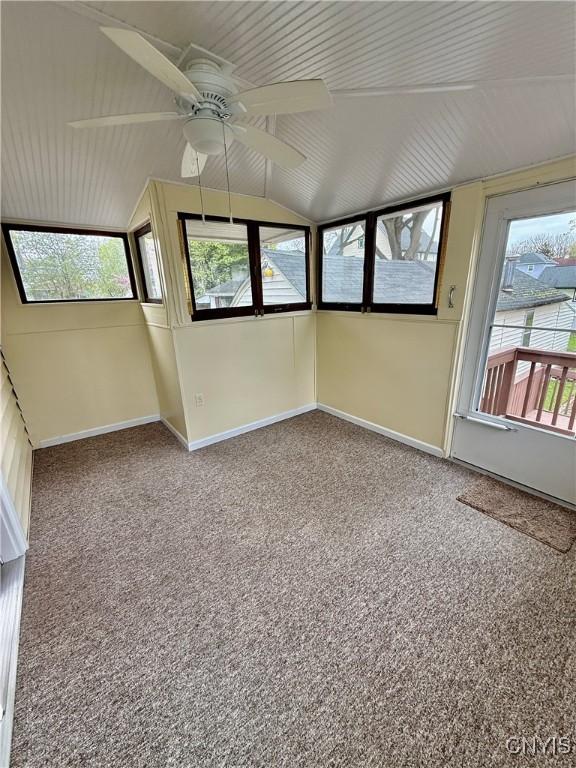 carpeted empty room featuring baseboards, vaulted ceiling, and ceiling fan