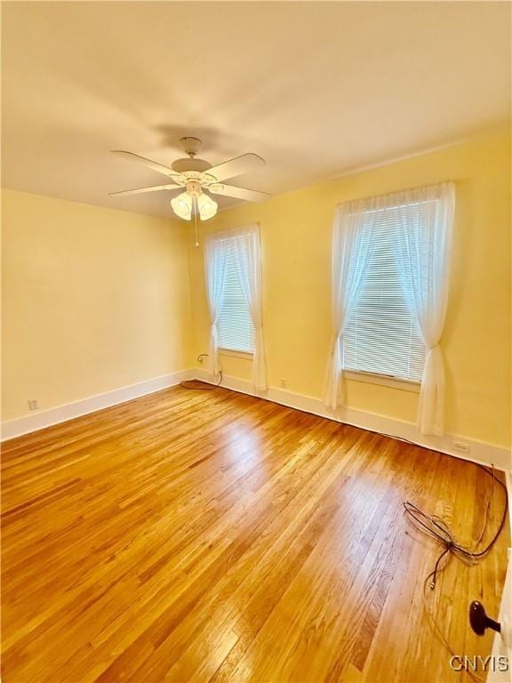empty room with baseboards, ceiling fan, and light wood-style floors
