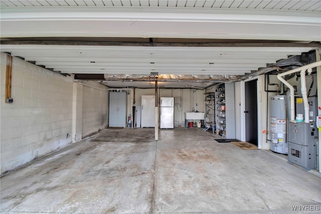 garage featuring a sink, gas water heater, freestanding refrigerator, and concrete block wall