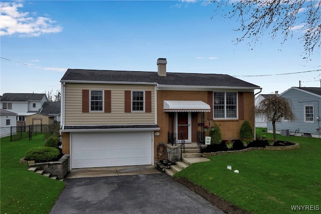 split foyer home featuring aphalt driveway, fence, a front yard, brick siding, and an attached garage