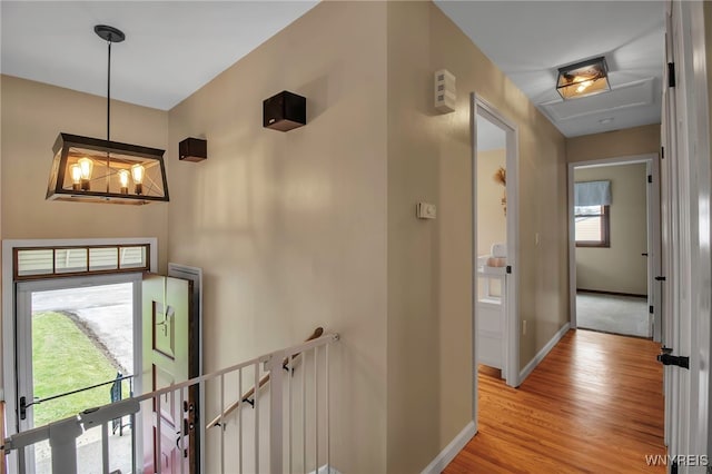 corridor with baseboards, a notable chandelier, an upstairs landing, and light wood-type flooring
