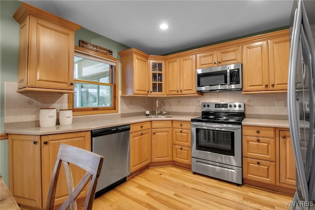 kitchen with decorative backsplash, light wood-style floors, light countertops, a sink, and stainless steel appliances