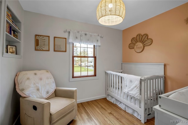 bedroom with baseboards, a crib, and wood finished floors