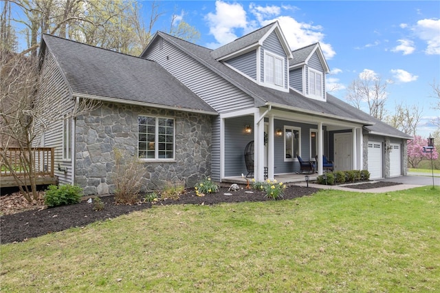 cape cod home featuring roof with shingles, a front lawn, stone siding, a garage, and a porch