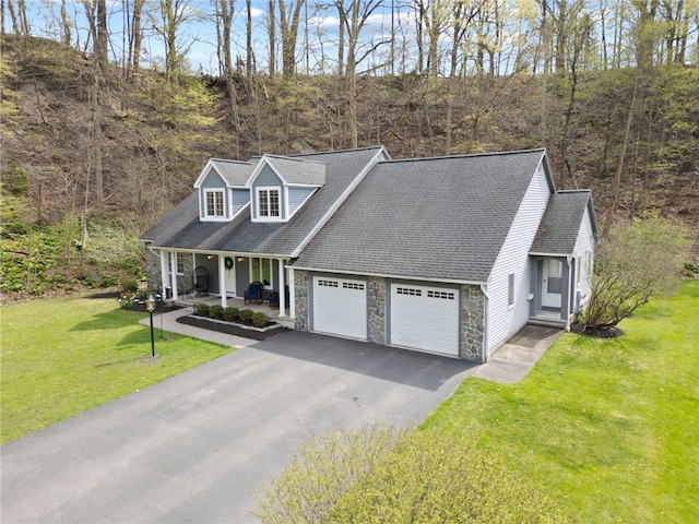 new england style home featuring an attached garage, a front lawn, stone siding, covered porch, and driveway