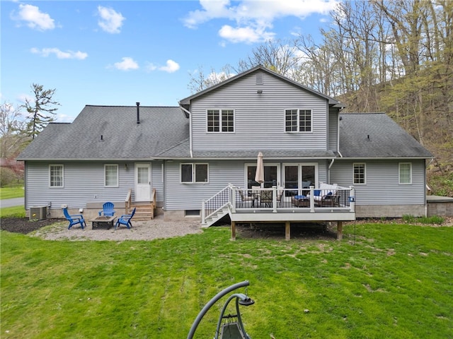 rear view of house with a shingled roof, an outdoor fire pit, a wooden deck, central air condition unit, and a yard
