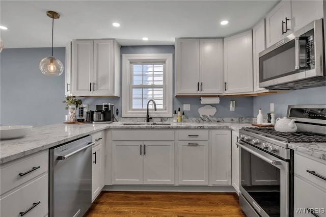 kitchen featuring dark wood-style floors, white cabinetry, a sink, appliances with stainless steel finishes, and hanging light fixtures