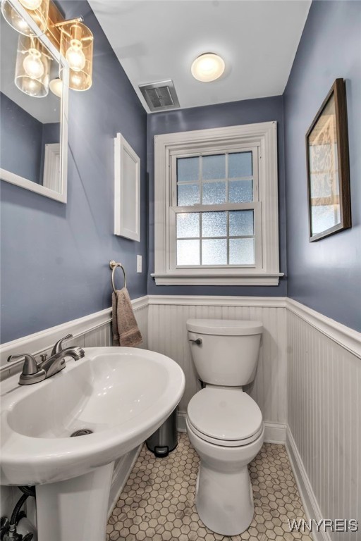 half bath with visible vents, wainscoting, a sink, tile patterned floors, and toilet