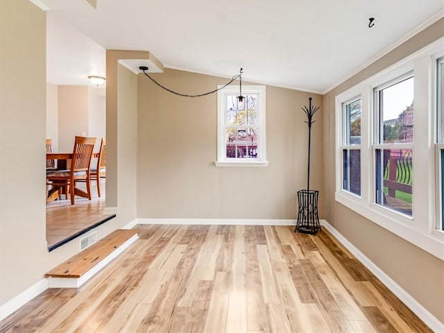 unfurnished dining area featuring baseboards, visible vents, ornamental molding, and wood finished floors