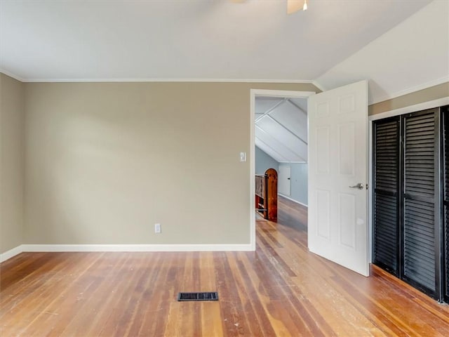 unfurnished bedroom featuring baseboards, vaulted ceiling, light wood-style flooring, and visible vents