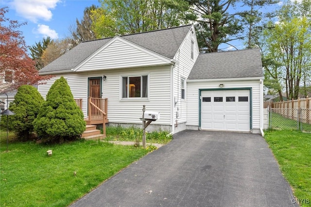 view of front of house with roof with shingles, fence, an attached garage, a front yard, and driveway