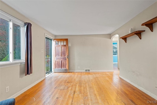 unfurnished room with visible vents, arched walkways, light wood-style flooring, and plenty of natural light