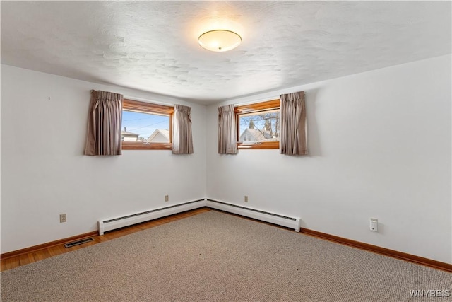 spare room with a textured ceiling, baseboards, wood finished floors, a baseboard radiator, and visible vents