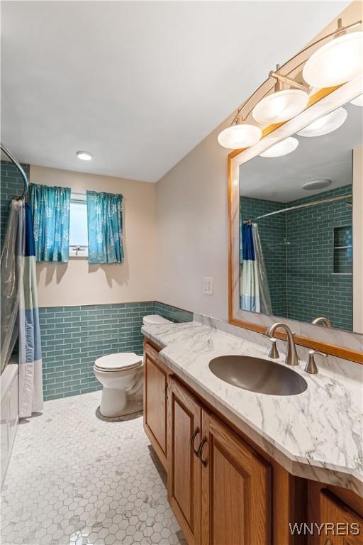 bathroom with tile walls, wainscoting, vanity, toilet, and shower / bathtub combination with curtain