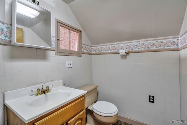 bathroom with vanity, toilet, a wainscoted wall, tile walls, and vaulted ceiling