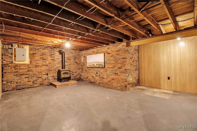unfinished below grade area featuring electric panel, a wood stove, and brick wall
