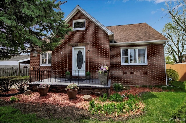 view of front facade with fence, a shingled roof, a front lawn, and brick siding