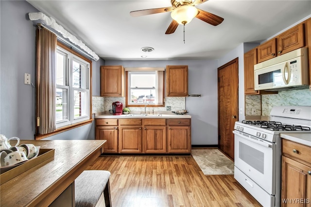 kitchen featuring white appliances, brown cabinets, a sink, and light wood finished floors