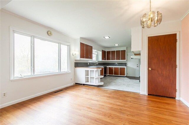 kitchen with light wood-style floors, a sink, baseboards, an inviting chandelier, and ornamental molding