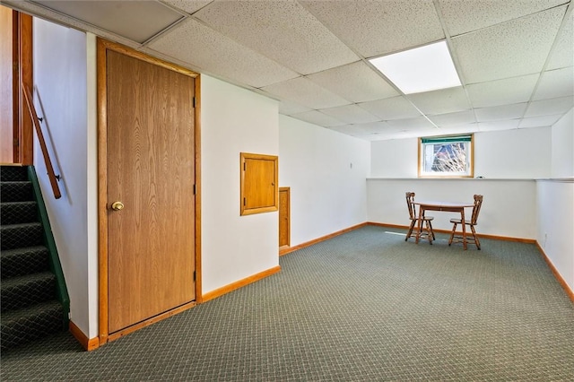 below grade area with baseboards, carpet, stairway, and a paneled ceiling