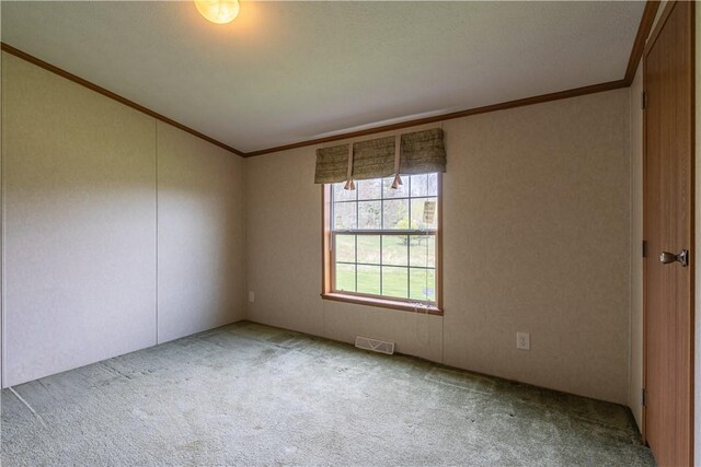 empty room featuring carpet floors, ornamental molding, visible vents, and vaulted ceiling