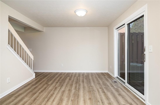 empty room with stairway, baseboards, wood finished floors, and visible vents