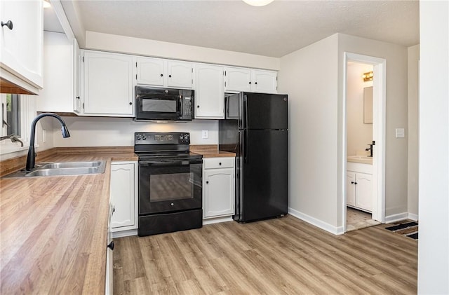kitchen with a sink, baseboards, white cabinets, black appliances, and light wood-style floors