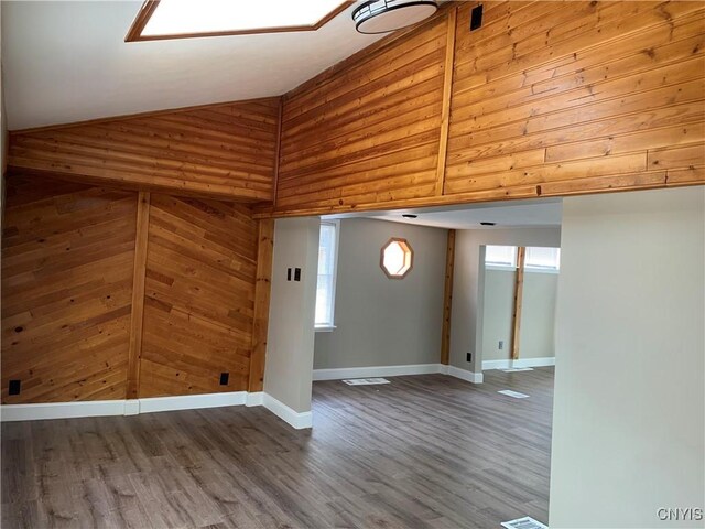 unfurnished room with wooden walls, high vaulted ceiling, baseboards, wood finished floors, and visible vents