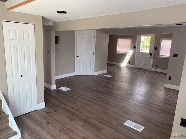 unfurnished living room featuring visible vents, baseboards, and dark wood-style floors