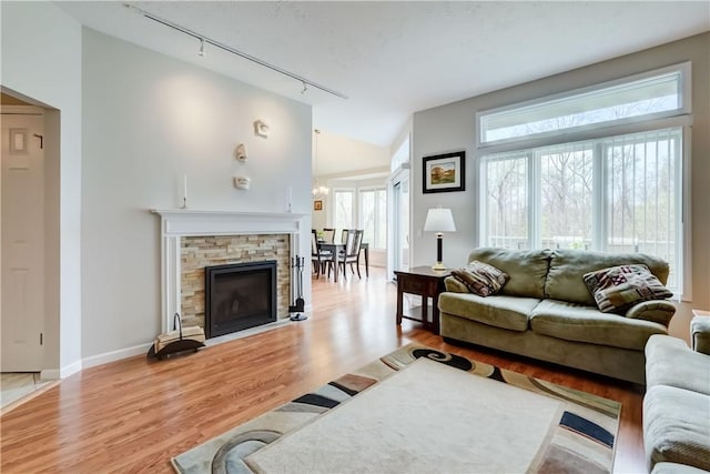 living area with an inviting chandelier, rail lighting, baseboards, light wood-type flooring, and vaulted ceiling