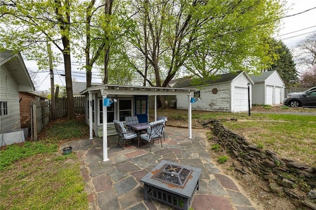 view of patio featuring a detached garage, fence, an outdoor structure, and an outdoor fire pit