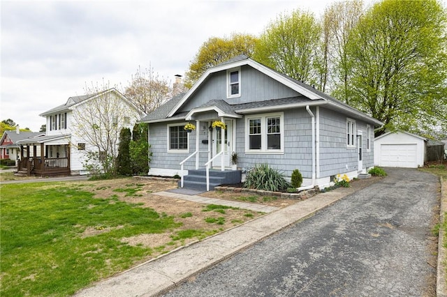 bungalow-style home with aphalt driveway, roof with shingles, a chimney, an outbuilding, and a detached garage