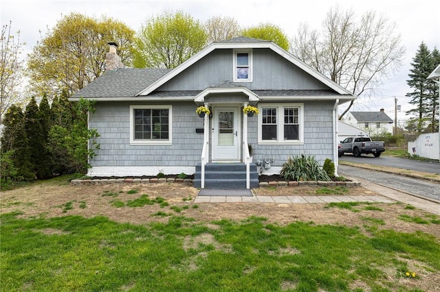 bungalow with a front lawn, roof with shingles, and a chimney