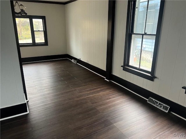 empty room featuring plenty of natural light, dark wood-style flooring, and visible vents