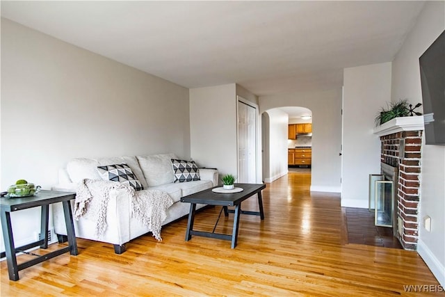 living area with baseboards, arched walkways, light wood finished floors, and a brick fireplace