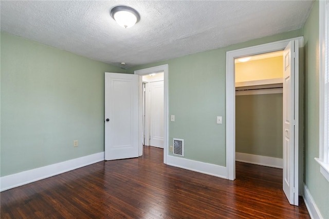 unfurnished bedroom with a textured ceiling, visible vents, baseboards, a closet, and dark wood-type flooring