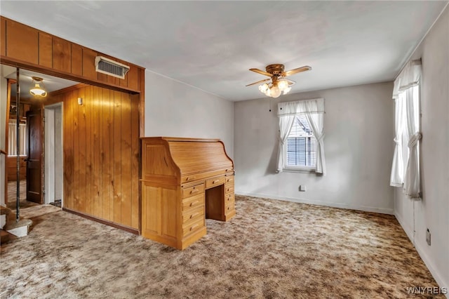 interior space featuring baseboards, a ceiling fan, wood walls, and visible vents