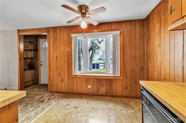 unfurnished dining area with a ceiling fan, baseboards, and wood walls