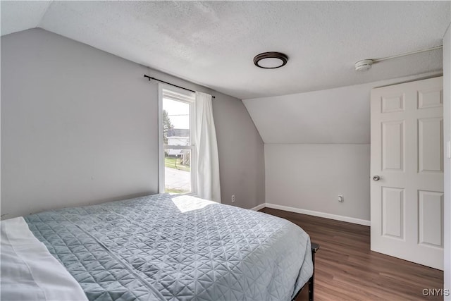 bedroom with a textured ceiling, baseboards, wood finished floors, and lofted ceiling