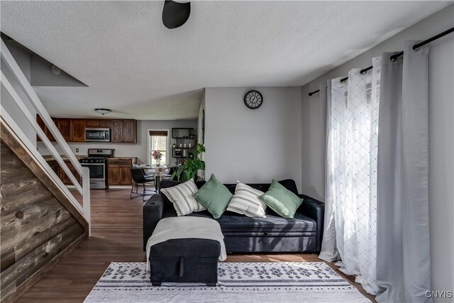 living room featuring a textured ceiling, dark wood finished floors, and stairway