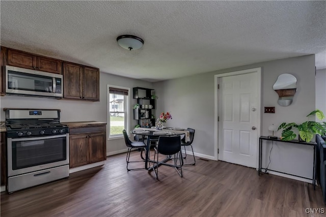 kitchen featuring a textured ceiling, appliances with stainless steel finishes, dark wood-style floors, and baseboards