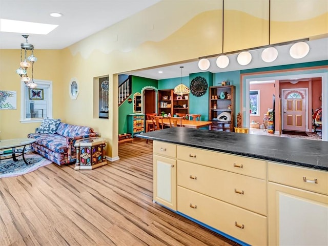 kitchen with pendant lighting, lofted ceiling, baseboards, light wood-type flooring, and cream cabinets