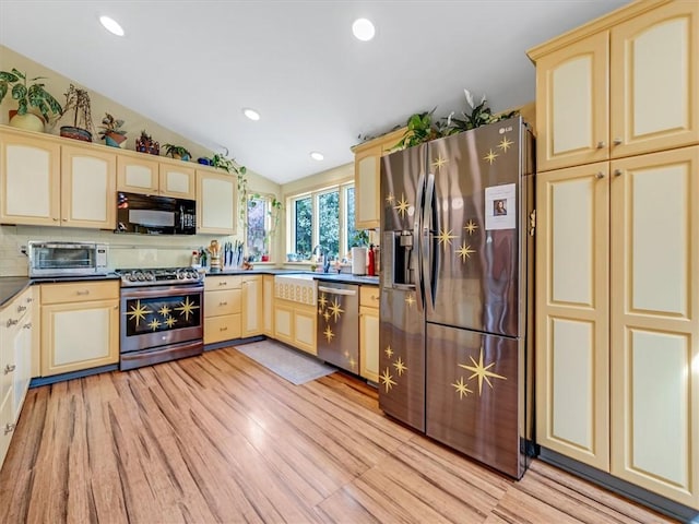kitchen with cream cabinets, stainless steel appliances, lofted ceiling, and light wood finished floors