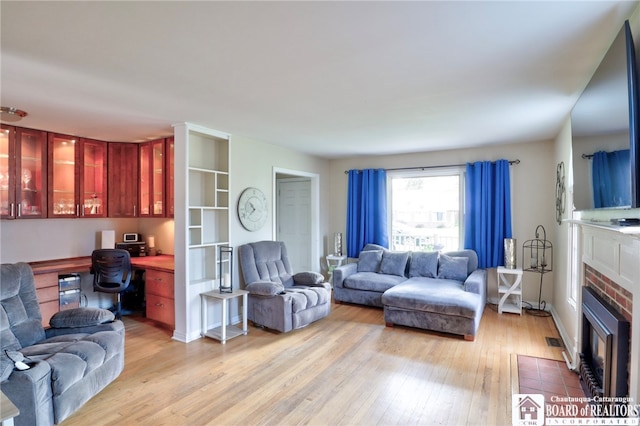living room with a fireplace with flush hearth, light wood finished floors, and built in desk
