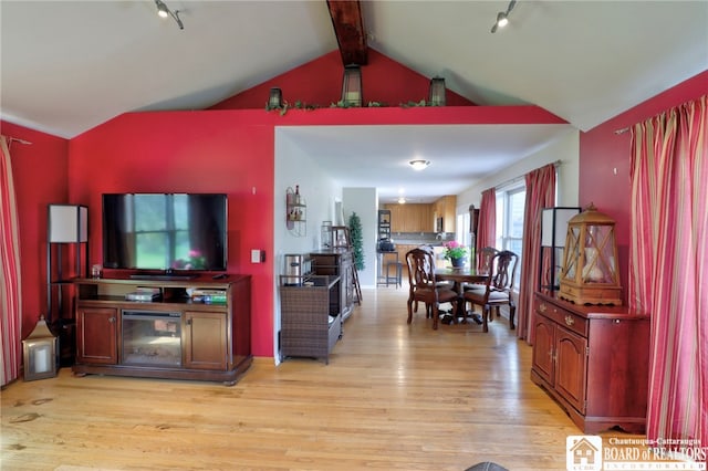 living room featuring track lighting, vaulted ceiling with beams, and light wood-style flooring