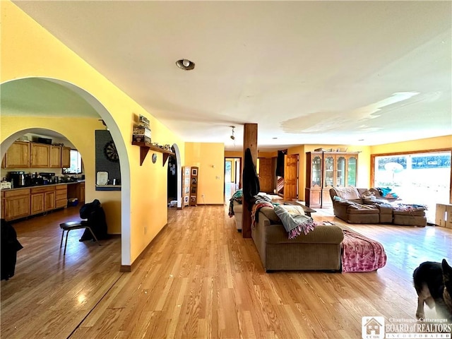 living room with arched walkways, light wood-style flooring, and a wealth of natural light
