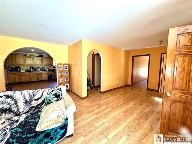 living area featuring arched walkways, baseboards, and light wood finished floors
